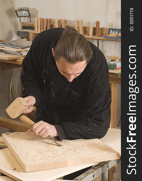 Carpenter cutting in his workshop with chisel and wooden hammer