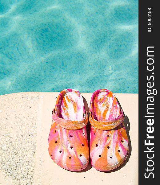 Brightly colored sandals by the side of swimming pool.