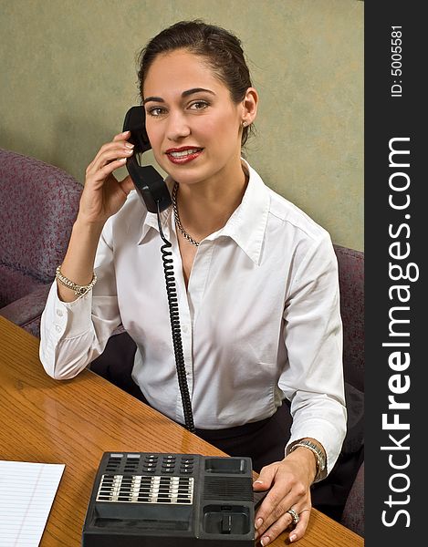A pretty brunette business woman is on the phone in her office. A pretty brunette business woman is on the phone in her office.