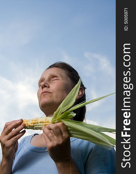 Middle adult woman with corncob in hands tasting it and enjoying.