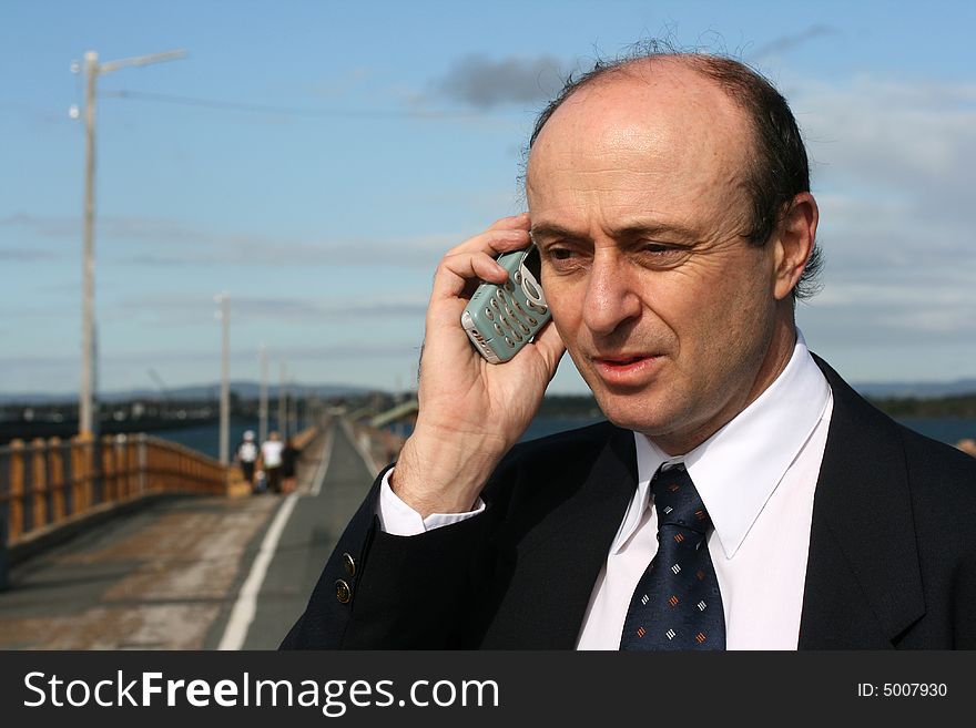 Businessman on his mobile telephone, with the straight road ahead of him going to a point in the distance, indicating which direction now for his business. Businessman on his mobile telephone, with the straight road ahead of him going to a point in the distance, indicating which direction now for his business