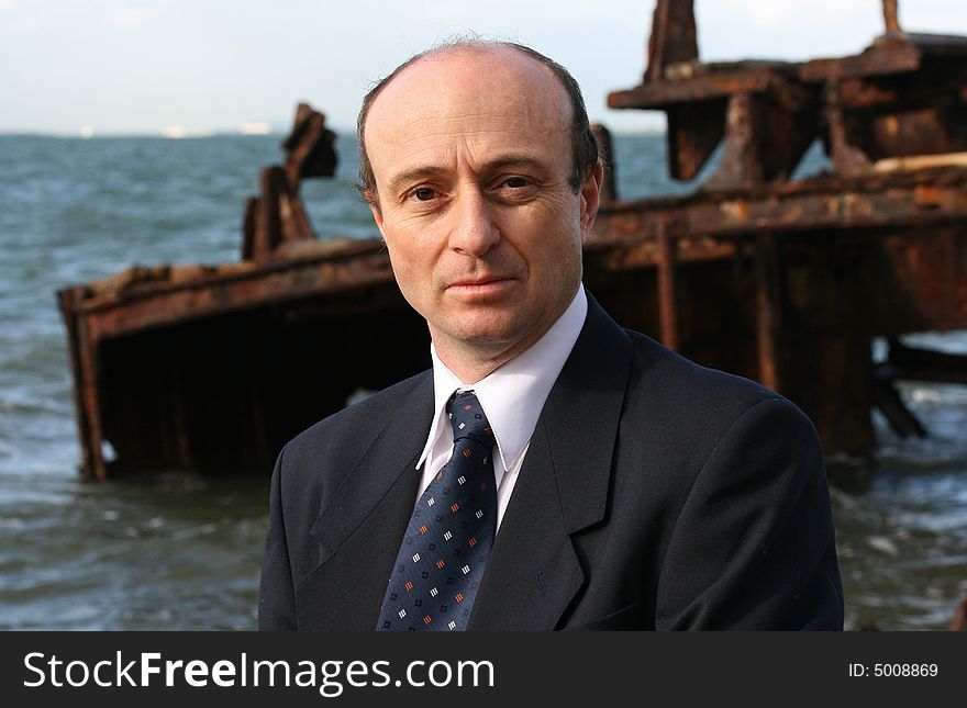 Businessman on the beach by an old wreck, dressed in business attire in front of a very old rusting shipwreck on the beach, with his briefcase and walking past rusting shipwreck thinking is this where my business will end up. Businessman on the beach by an old wreck, dressed in business attire in front of a very old rusting shipwreck on the beach, with his briefcase and walking past rusting shipwreck thinking is this where my business will end up