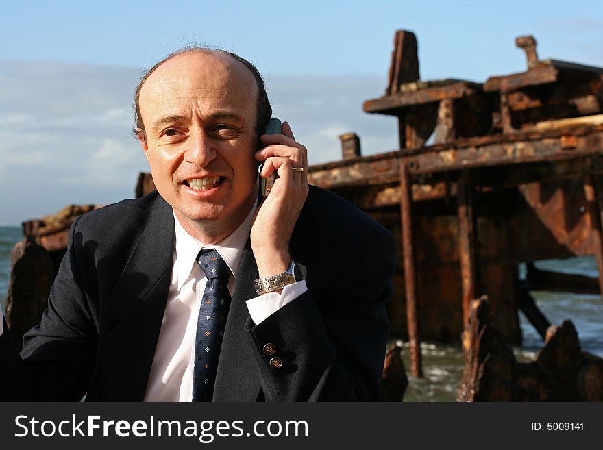 Businessman explaining on his mobile telephone that the shipwreck cannot be salvaged, as it had run aground years ago,. Businessman explaining on his mobile telephone that the shipwreck cannot be salvaged, as it had run aground years ago,