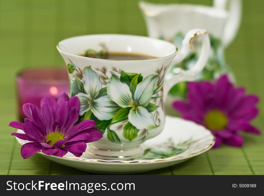 Cup of coffee with creamer, flowers and candle on green background. Cup of coffee with creamer, flowers and candle on green background