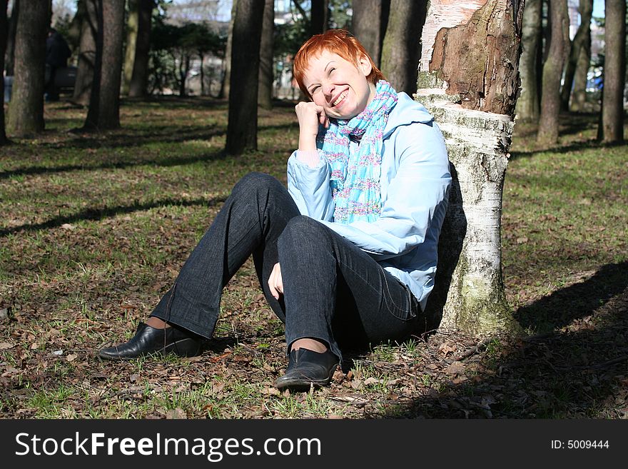 Red haired woman is sitting near tree