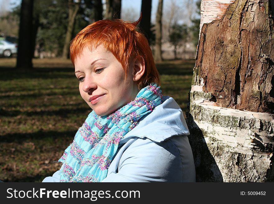 Red haired woman is sitting near tree