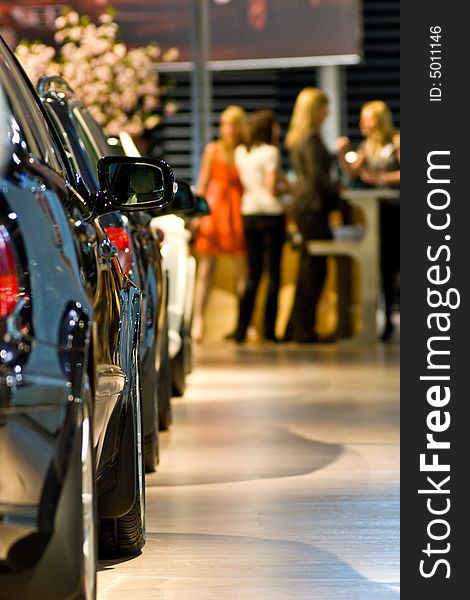 Row of new cars at this year's biggest motorshow in the Baltics. Visitors consulting sales department in the background. Row of new cars at this year's biggest motorshow in the Baltics. Visitors consulting sales department in the background.