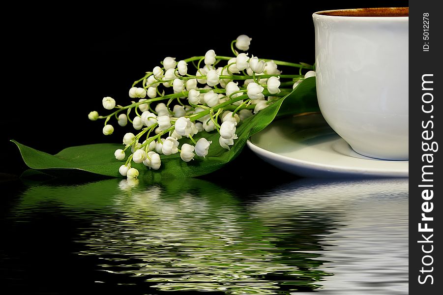 Flowers of a llies of the valley and white cup of black coffee on a black background. Flowers of a llies of the valley and white cup of black coffee on a black background