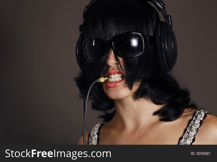 Girl with headphones and sunglasses biting cable plug