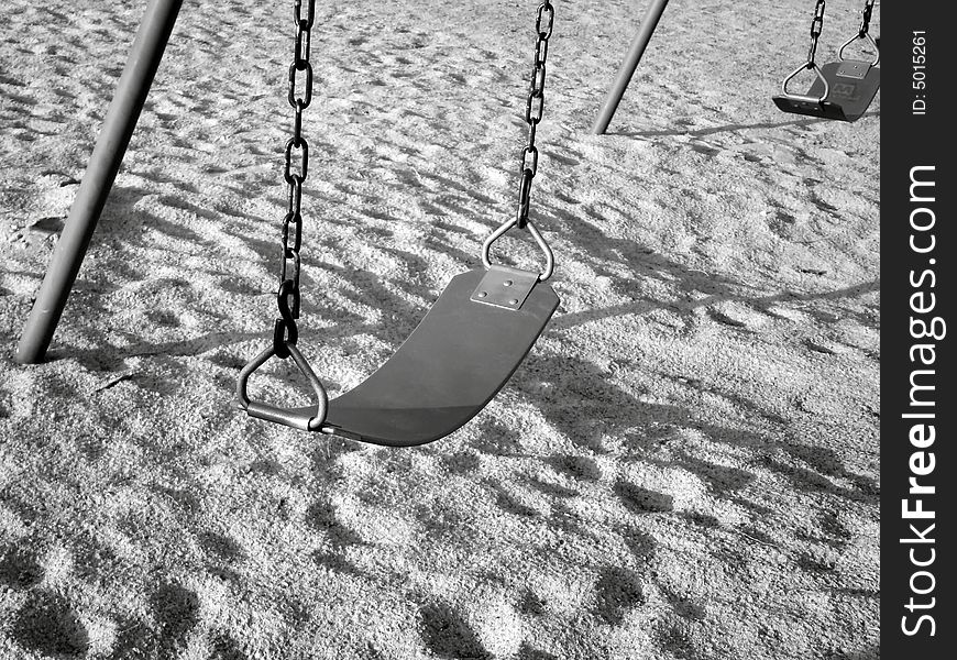 Black/white image of swing seats on playground in a park