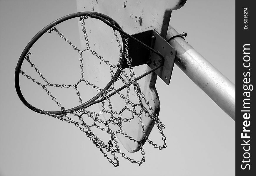 Black and white image at a slant of basketball hoop and backboard on playground