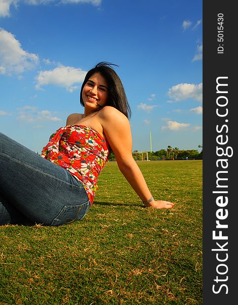 Woman sitting on a field of grass with blue sky background. Woman sitting on a field of grass with blue sky background