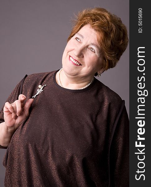 The cheerful elderly woman in a brown dress on a grey background. The cheerful elderly woman in a brown dress on a grey background.