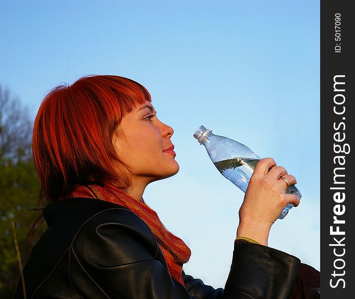 The beautiful young girl drinks water on a background of the sky