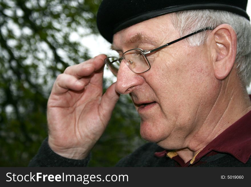 A senior with glasses and flatcap with his hand up to his face. A senior with glasses and flatcap with his hand up to his face