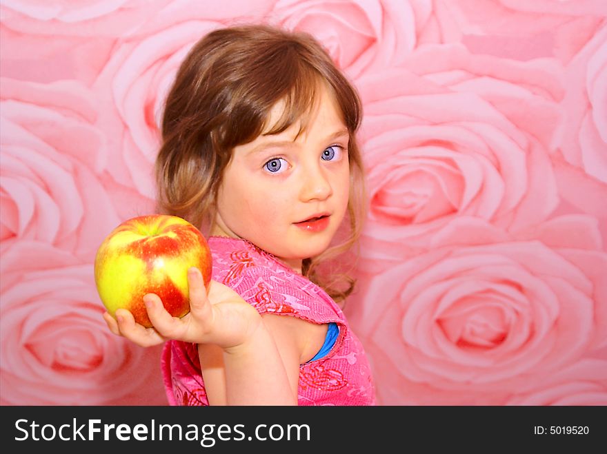 In the hands of the child's great apple. The girl stands with pink walls and she dressed in a pink blouse.