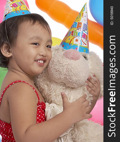 Young girl holding teddy bear with party hat