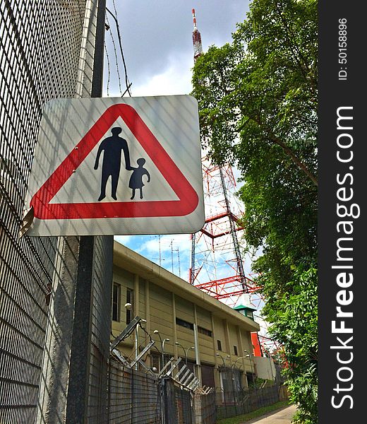 A signboard showing parent holding child's hand to remind pedestrians to look after the younger ones when crossing or walking along the road around Bukit Batok Nature Park. A signboard showing parent holding child's hand to remind pedestrians to look after the younger ones when crossing or walking along the road around Bukit Batok Nature Park