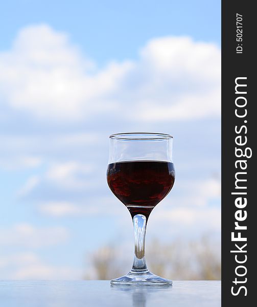 Nice goblet of red wine on background with blue sky and clouds. Nice goblet of red wine on background with blue sky and clouds