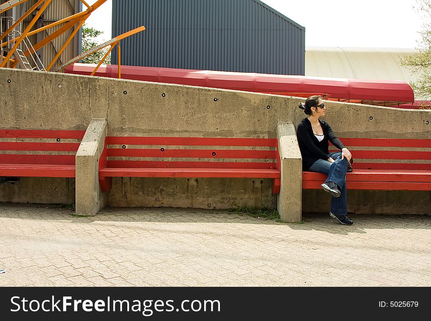 Beautiful young woman sitting/waiting on a red bench on a bright day, wearing sunglasses. Beautiful young woman sitting/waiting on a red bench on a bright day, wearing sunglasses
