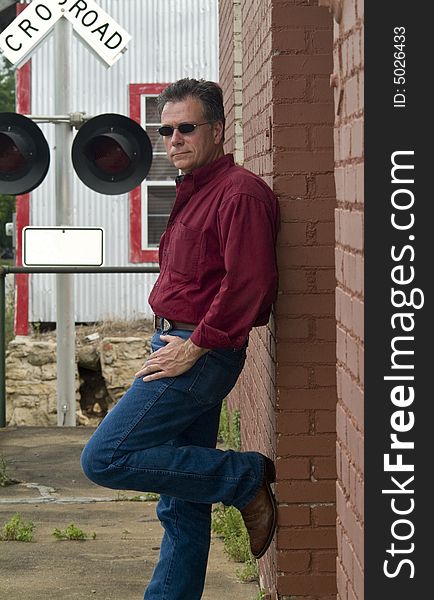 A man leaning up against a red brick wall with a railroad crossing warning signal in the background. A man leaning up against a red brick wall with a railroad crossing warning signal in the background.