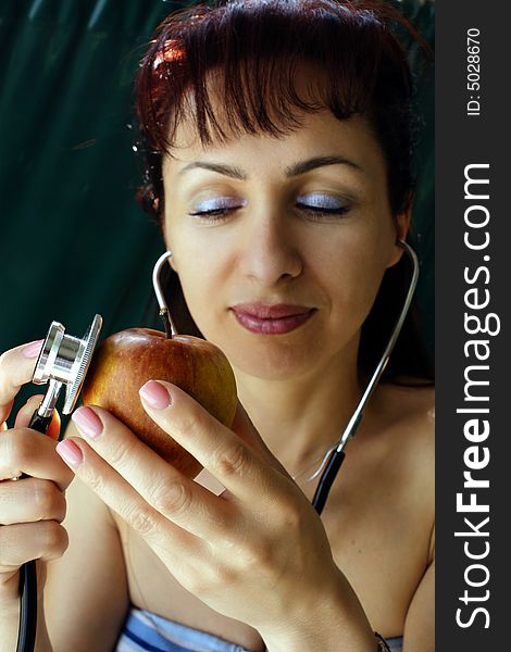 Young woman examining an apple by using a stethoscope. Young woman examining an apple by using a stethoscope