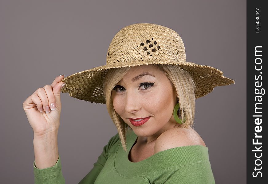 A young blonde in a green blouse and a straw hat holding the brim. A young blonde in a green blouse and a straw hat holding the brim