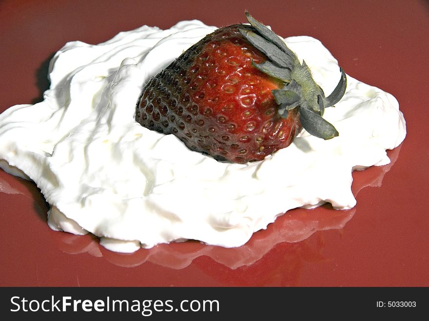 A strawberry on a bed of whipped cream on a red plate. A strawberry on a bed of whipped cream on a red plate.