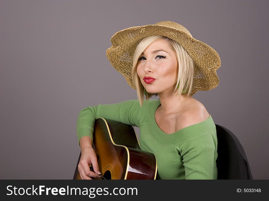 A blonde in a green blouse playing the guitar and puckering her lips. A blonde in a green blouse playing the guitar and puckering her lips