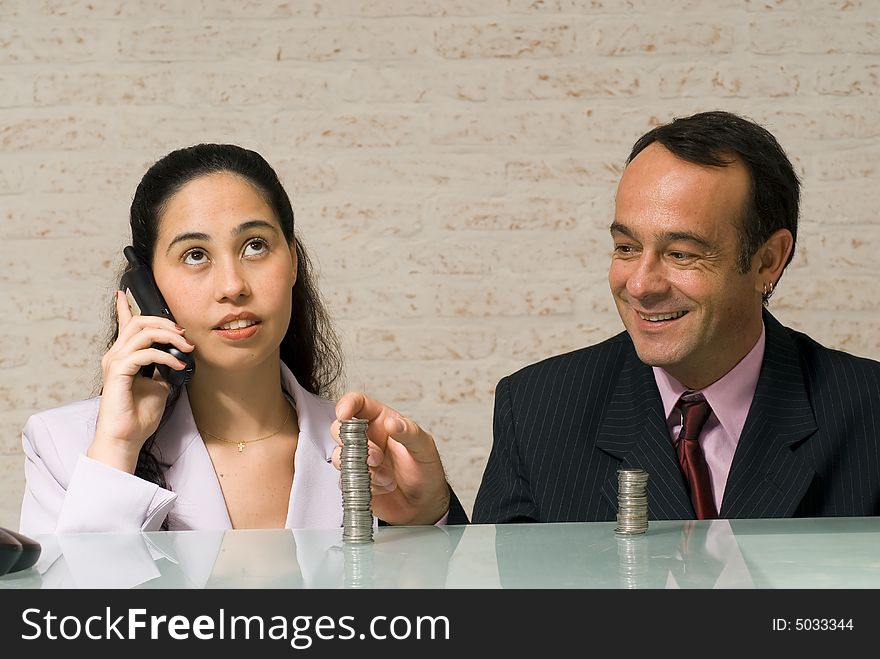 Businessman reaching over and stealing money playfully from his female colleague while she talks on the phone. Businessman reaching over and stealing money playfully from his female colleague while she talks on the phone