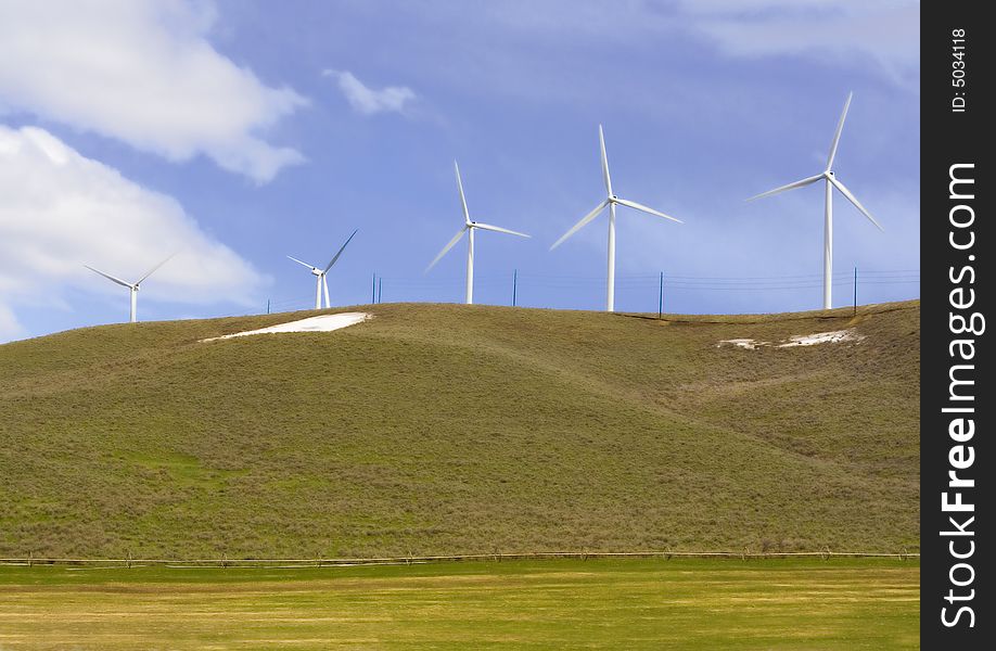 Five modern windmills sit on top of a green hill in spring. Five modern windmills sit on top of a green hill in spring.