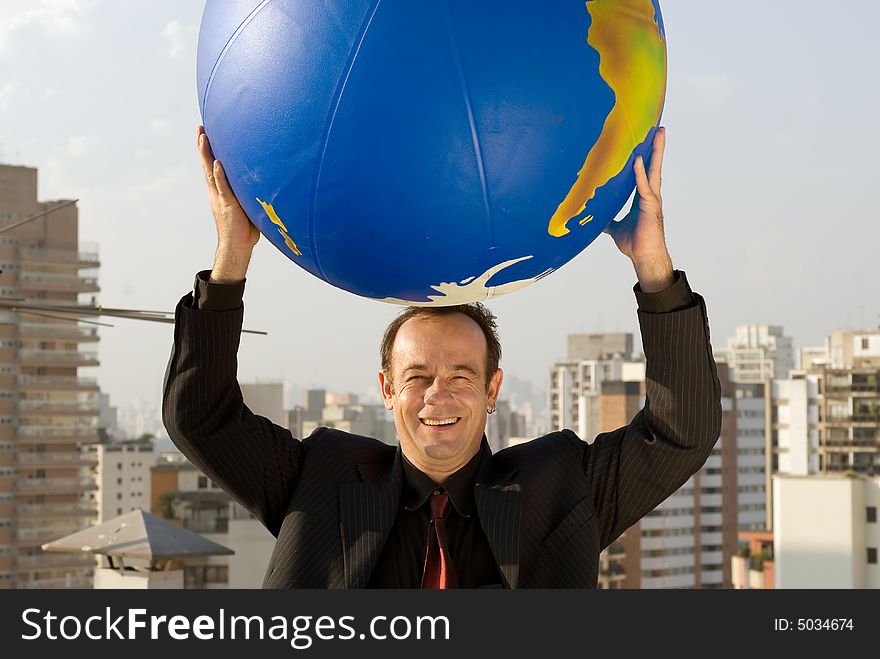 A businessman holding a large globe of the Earth in both hands above his head. A businessman holding a large globe of the Earth in both hands above his head.