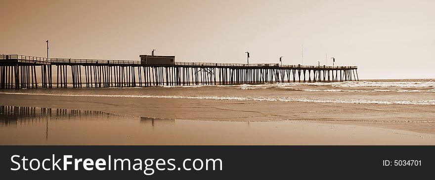 A pier extending out into the pacific ocean with the reflection on the beach. A pier extending out into the pacific ocean with the reflection on the beach