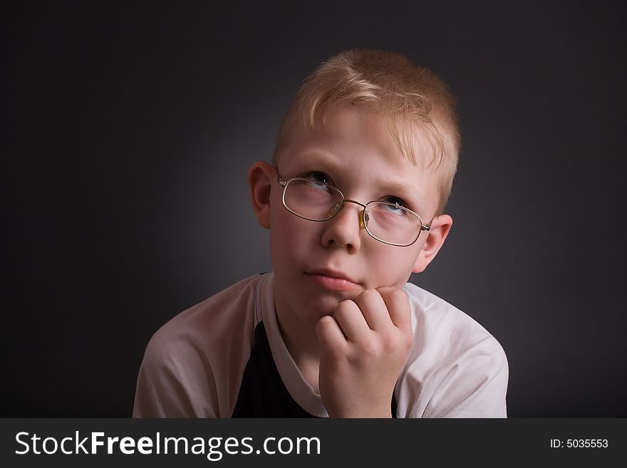 Boy look up and prop his head by hand in puzzlement as if pondering a deep question. Over grey background.