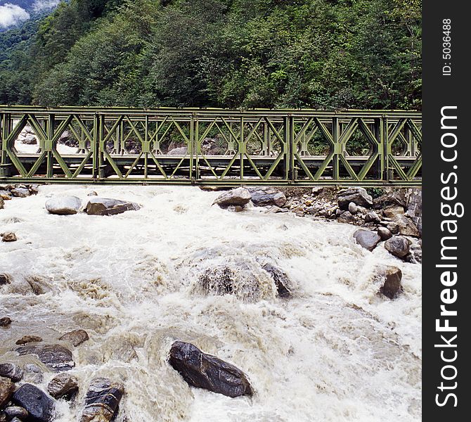 It is a metal bridge on the river, it is in Tibet of China. with green forest.