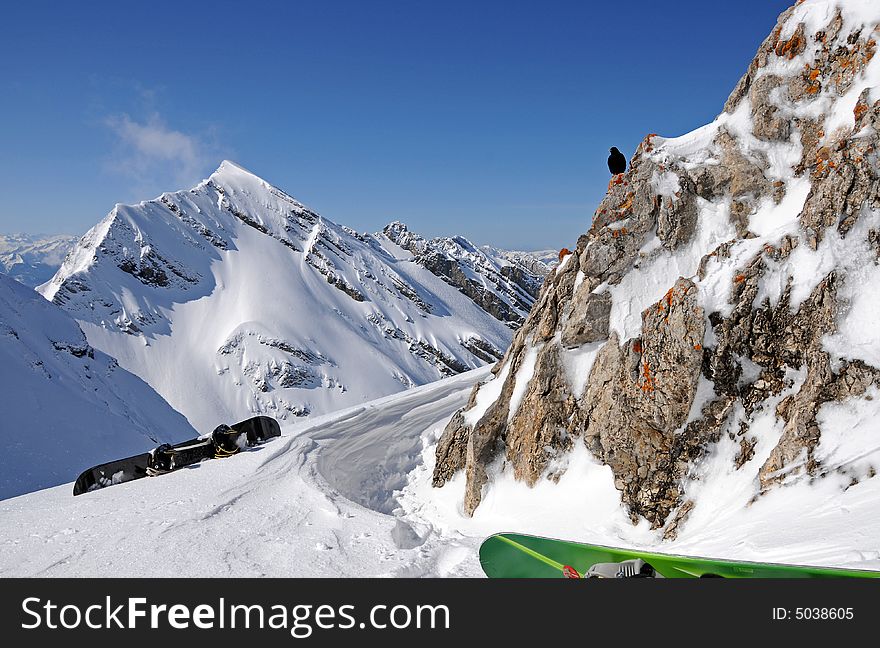 Winter mountain scenery with two snowboards and black bird on the rock. Winter mountain scenery with two snowboards and black bird on the rock