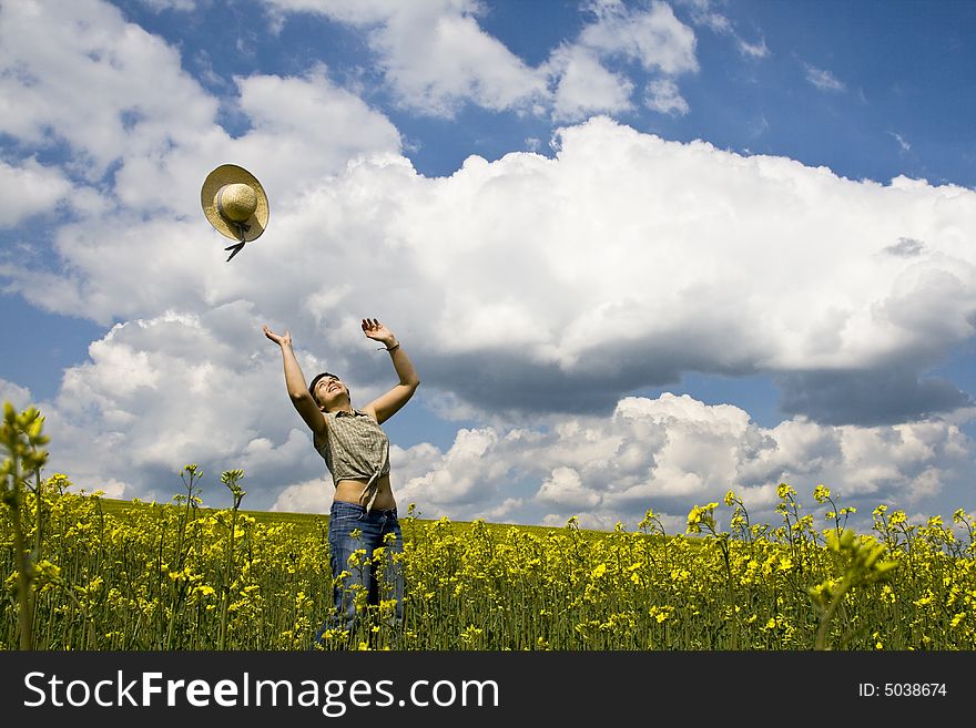 Young attractive girl jumping in rape field and throwing straw hat. Young attractive girl jumping in rape field and throwing straw hat