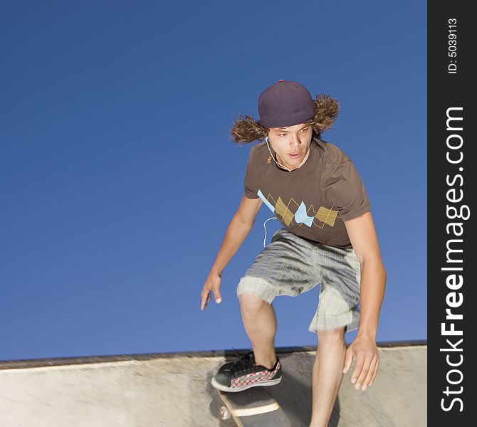 Teen boy rides down the side of a half pipe at a skate park. Teen boy rides down the side of a half pipe at a skate park