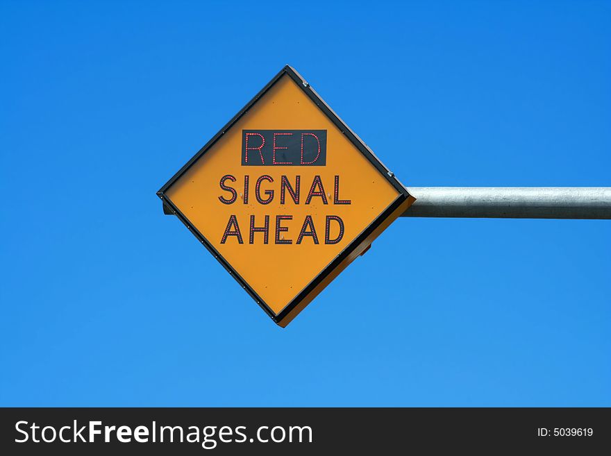 A Red signal ahead sign against blue sky