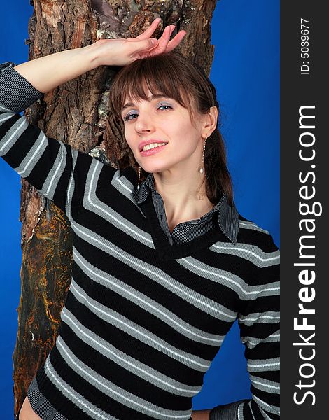 Portrait of a young woman standing near a tree. At the blue background. Portrait of a young woman standing near a tree. At the blue background.