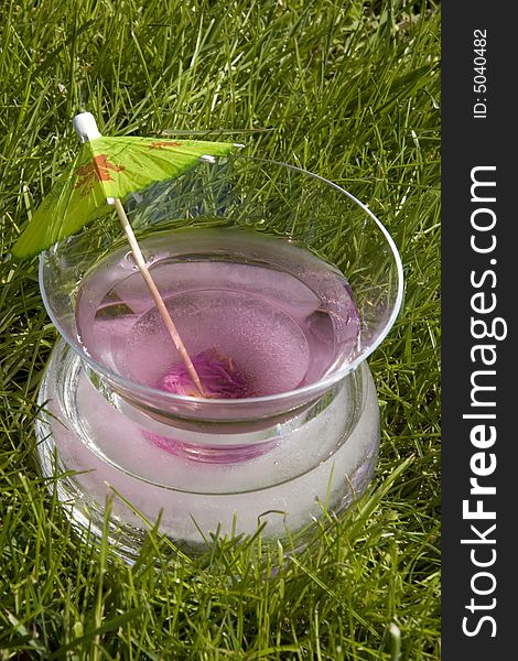 A Cosmopolitan Martini in a glass with a frozen rose sits in the grass. A Cosmopolitan Martini in a glass with a frozen rose sits in the grass.