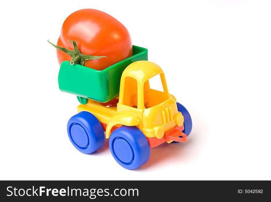 A photo of a little toy lorry carrying a tomato. A photo of a little toy lorry carrying a tomato