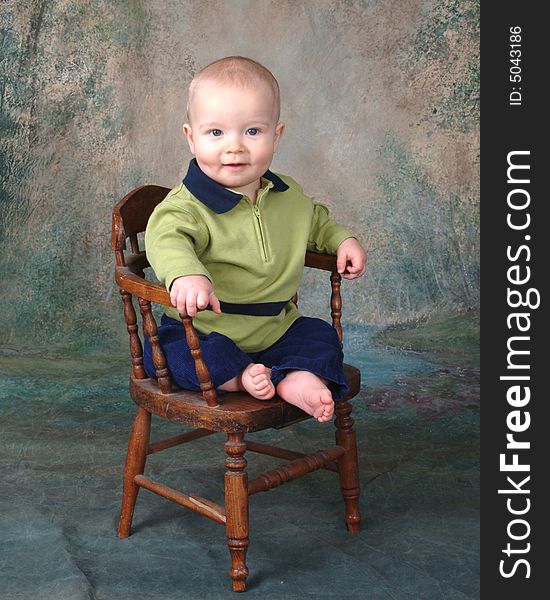 Baby boy sitting in front of muslin background on old wooden chair. Baby boy sitting in front of muslin background on old wooden chair