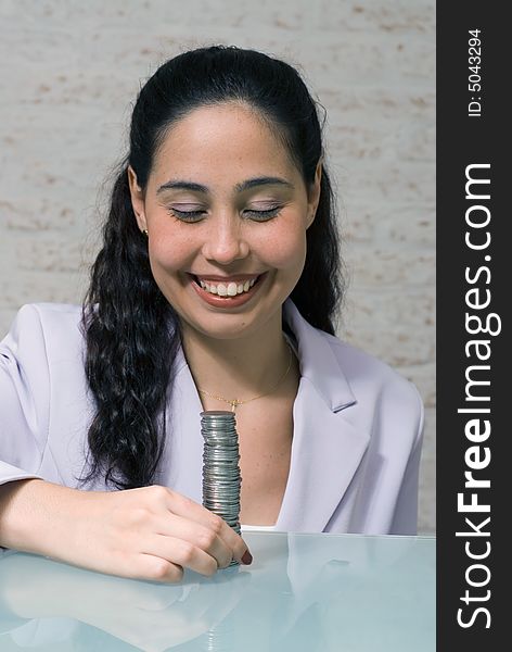 Latin american woman in a business suit with a big smile on her face looking at a big stack of coins. Latin american woman in a business suit with a big smile on her face looking at a big stack of coins