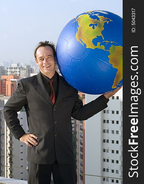 A businessman holding a large globe in one hand with his other hand on his hip. A businessman holding a large globe in one hand with his other hand on his hip.