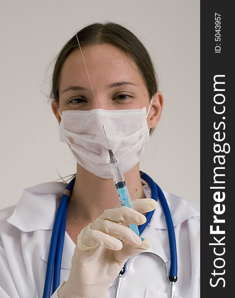 Young female doctor wearing a surgical mask and holding a syringe in the air. Young female doctor wearing a surgical mask and holding a syringe in the air