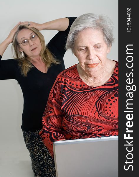 Woman looking over her elderly mother's shoulder while the older lady is working on a laptop. Woman looking over her elderly mother's shoulder while the older lady is working on a laptop