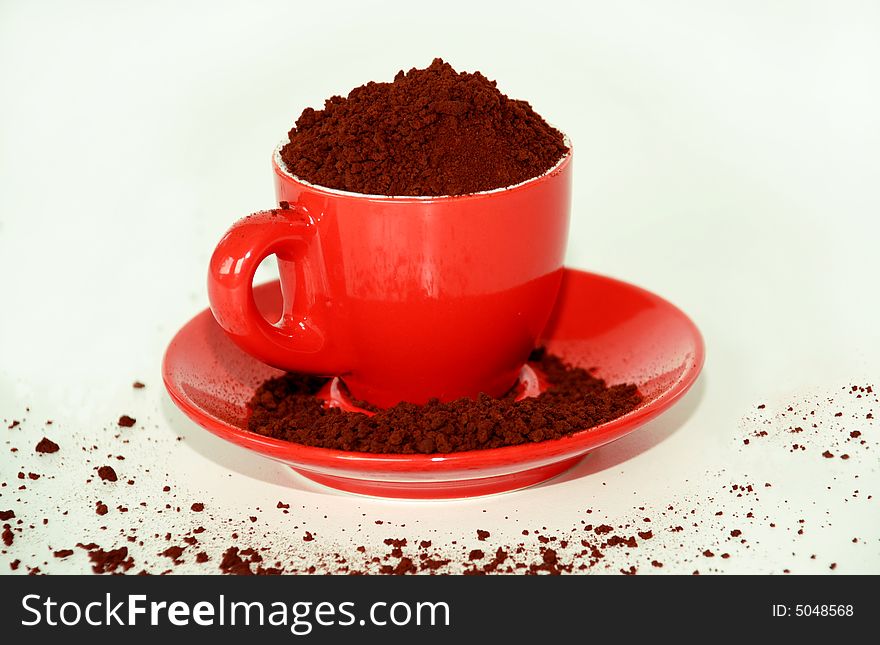 Red cup and saucer overfilled with coffee granules. Red cup and saucer overfilled with coffee granules