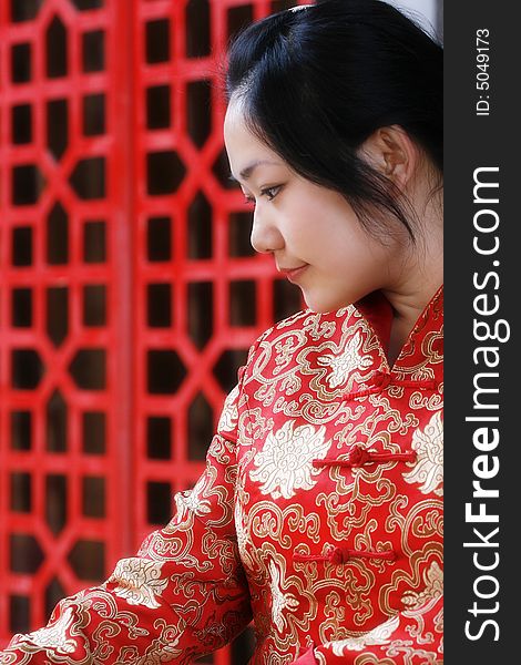 A Chinese girl in traditional dress ponders in front of the ancient window.