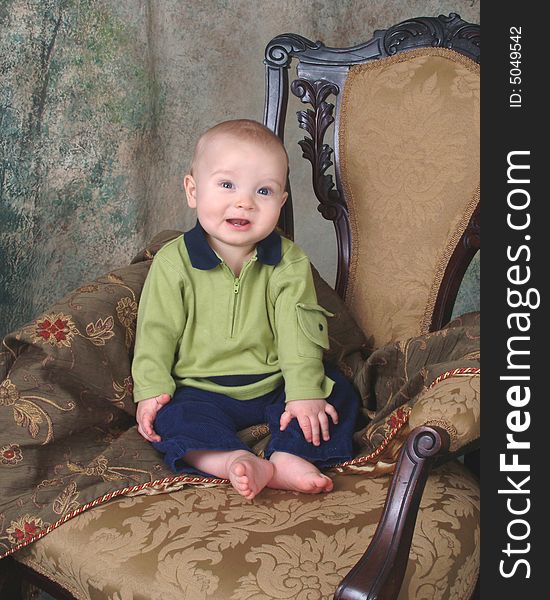 Baby boy sitting in front of muslin background on old antique chair. Baby boy sitting in front of muslin background on old antique chair